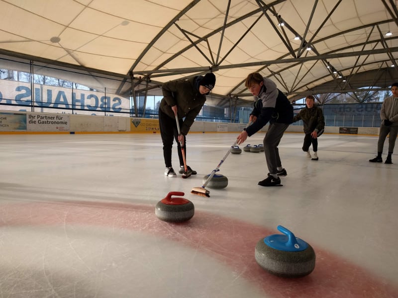 Schüler mit Besen in der Hand spielen Curling
