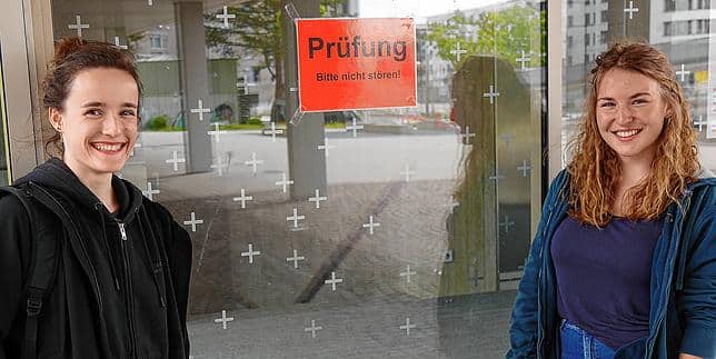 zwei Mädchen vor einer Glasscheibe auf der ein Schild mit "Prüfung" angebracht ist